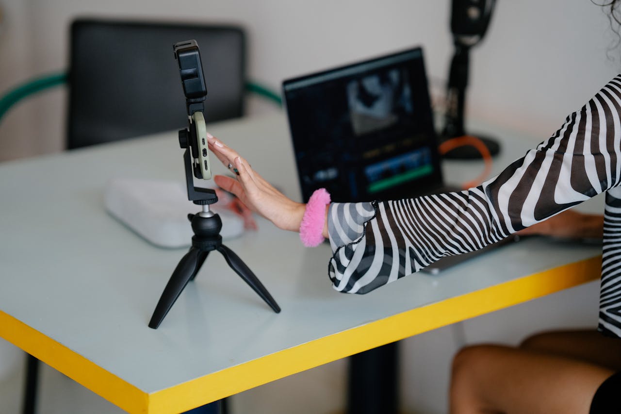 about-01 Woman adjusting smartphone on tripod with laptop setup for video editing.
